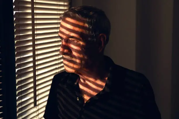 Photo of Man stares out the window through the blinds