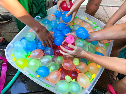 Children reach in and grab water balloons from a bucket full of balloons.