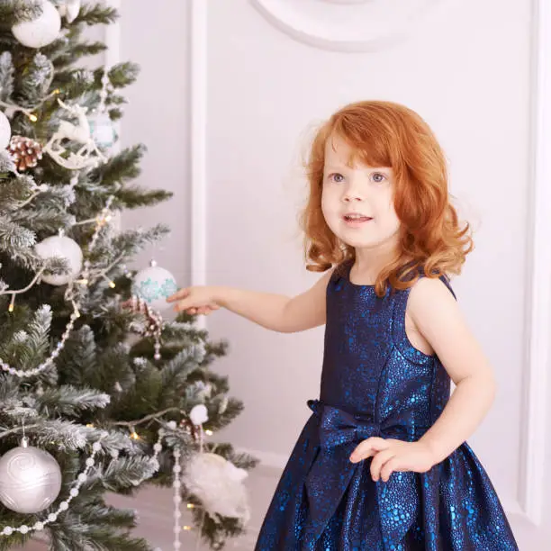 Little girl decorate tree. Christmas interior. Blue dress.