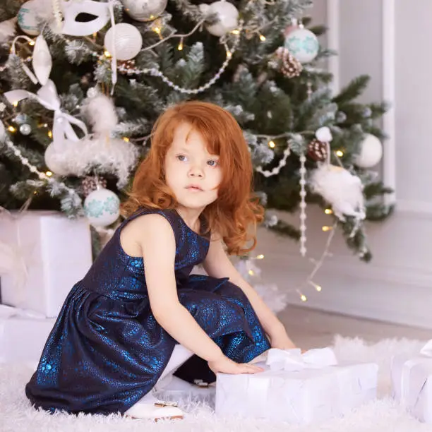 Little red hair girl. White background. Blue dress. Christmas gift.