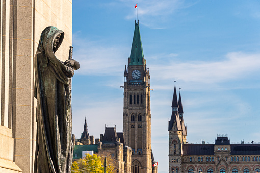 Ottawa, CA - 9 October 2019: Statue Ivstitia (Justice) in front of court Supreme of Canada with Canadian Parliament in background. The statue was made by canadian artist Walter S. Allward circa 1920