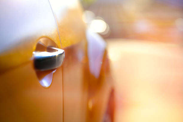 A classic orange car is parked along a tranquil street, with its shiny side mirror reflecting lush green trees and warm sunlight. The setting showcases a peaceful atmosphere and vintage charm.