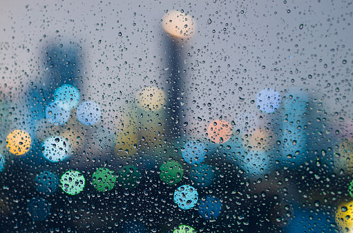 Rain drop on glass window in monsoon season with colorful bokeh light from city buildings background.