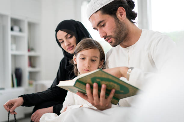 giovani genitori del golfo con figlio piccolo che legge il corano nel ramadan - saudi arabia child ramadan offspring foto e immagini stock