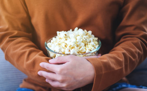istock a woman holding a bowl of pop corn while sitting on sofa at home 1248391809