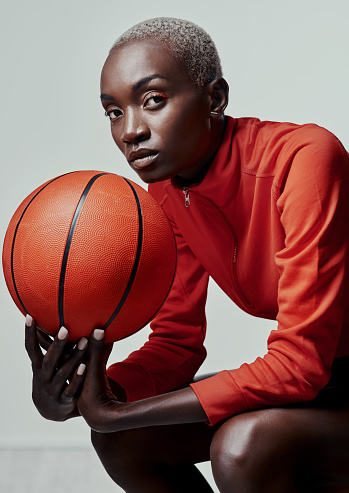 Studio shot of an attractive young woman playing basketball against a grey background