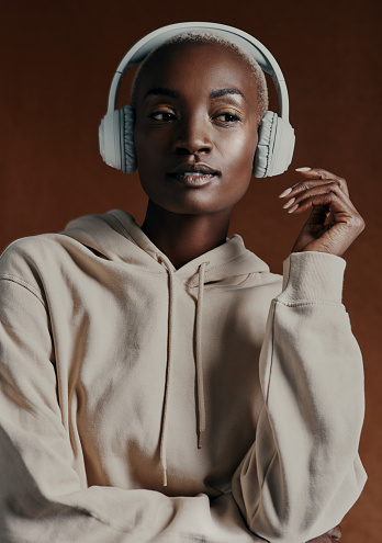 Studio shot of an attractive young woman wearing headphones and posing against a brown background