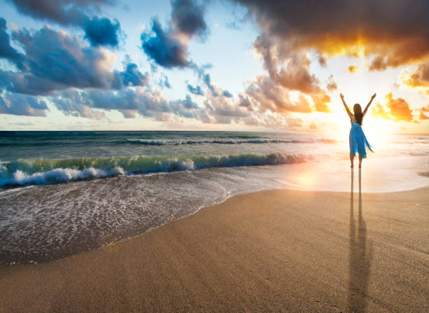 istock Woman with arms raised standing against sunset on beach 1248409156