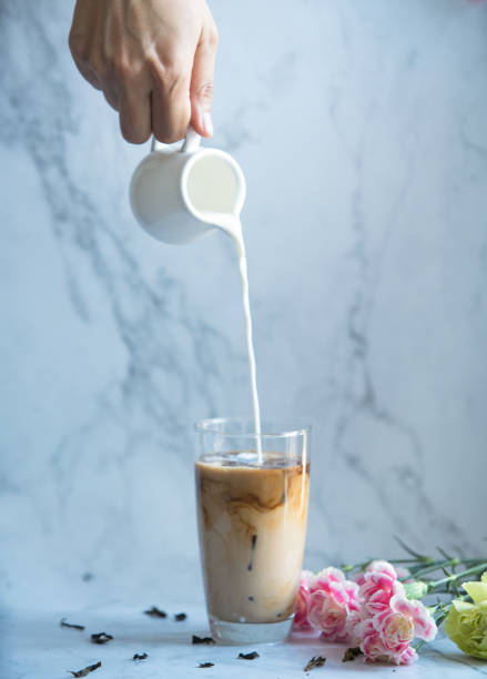 Thai milk tea. Pouring milk from jar to a cup of ice tea or coffee. Ice tea with carnation on the marble background. Thai milk tea. Pouring milk from jar to a cup of ice tea or coffee. Ice tea with carnation on the marble background. tea with milk stock pictures, royalty-free photos & images