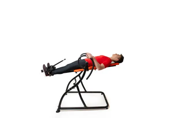 Photo of Man doing exercise on inversion table for his back pain, isolated on white