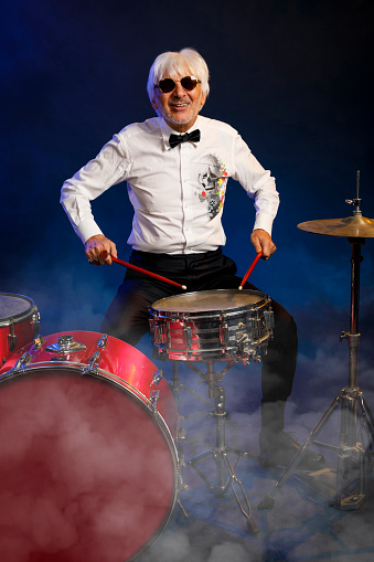 Musician Drummer Active senior Handsome man playing drum set. Blue  background, with rays of light and special effects smoke.