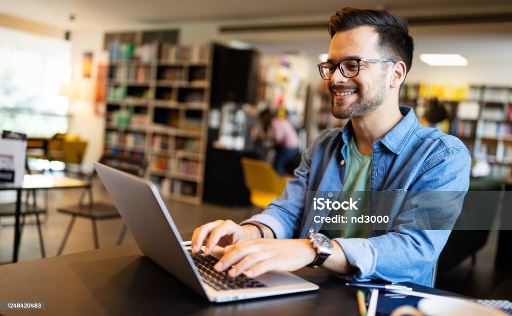 Lächelnde männliche Studenten, die in einer Bibliothek arbeiten und studieren - Lizenzfrei Akademisches Lernen Stock-Foto