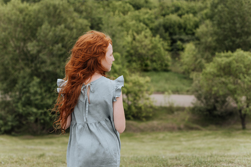 A redheaded girl looks into the distance her hair blowing in the wind.