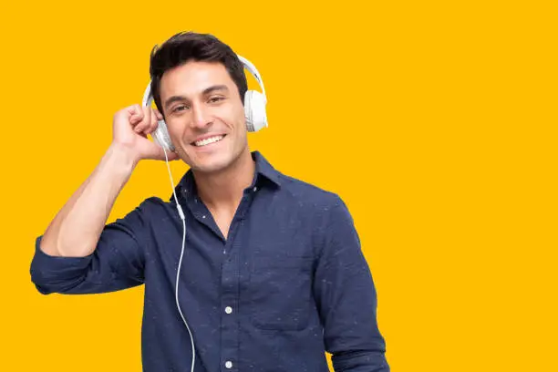 Photo of Young man listening music with headphones in playlist song application isolated on yellow background