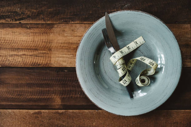 fourchette et couteau attachés avec un ruban à mesurer dans une assiette - healthy eating fork tape measure still life photos et images de collection