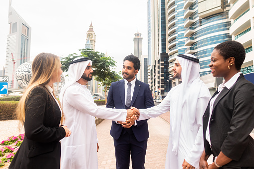 two diverse delegates shaking hands after agreement in the presence of arabic sheikh during meeting in boardroom. international business concept