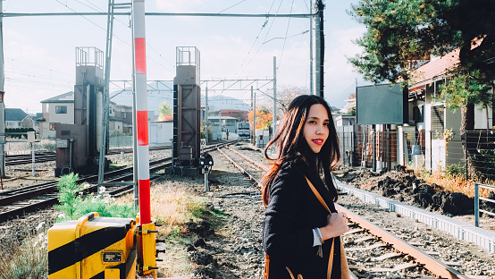 A side portrait of young Asian woman traveler is walking across the railway where is located in Fuji-Kawaguchiko, Yamanashi, Japan