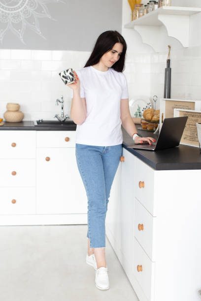 young happy woman drinking coffee and work on laptop in kitchen in the morning - working at home domestic kitchen laptop contemporary imagens e fotografias de stock