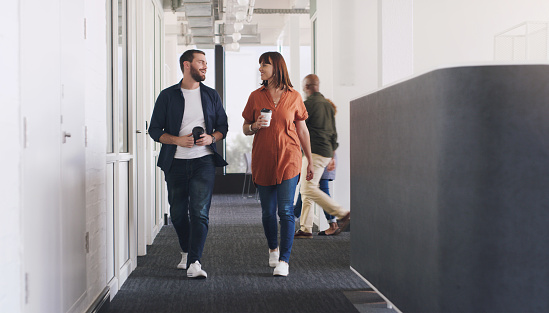 Shot of two businesspeople drinking coffee while walking through a corridor in an office together
