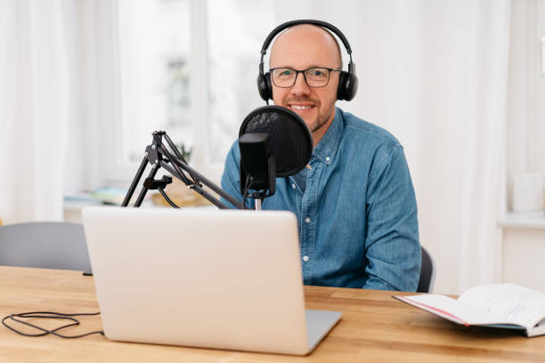 istock Man smiling at the camera as he sits recording 1248449644