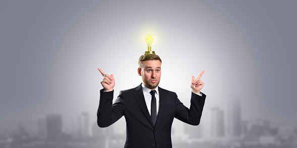 Business concept idea and innovation. Businessman with a light bulb over his head and points his hands up on a gray background with a copy space