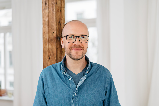 Happy friendly balding middle-aged man wearing glasses looking at the camera with a warm smile indoors with copy space