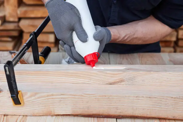 Male carpenter hands using wood glue and timber on a wooden table for handmade furniture. Close up. Hobby for man. Wooden table.