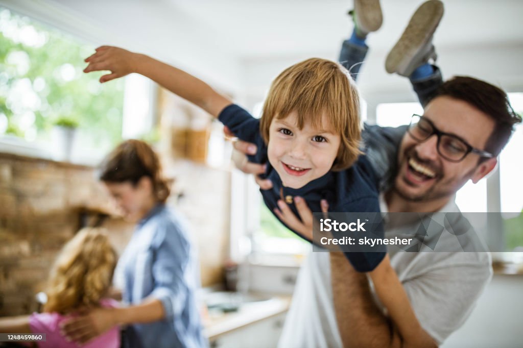Happy boy having fun with his father in the kitchen. Happy little boy having fun with his father at home and looking at camera. There are people in the background. Family Stock Photo