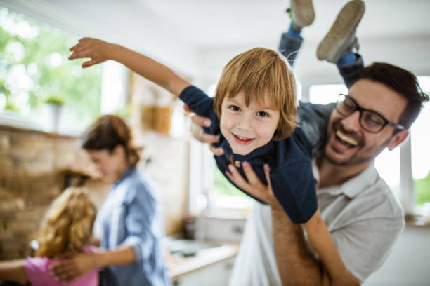 Happy boy having fun with his father in the kitchen. Happy little boy having fun with his father at home and looking at camera. There are people in the background. weekend activities photos stock pictures, royalty-free photos & images