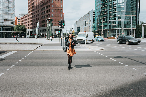 young black business woman with laptop crossing road at Potsdamer Platz in Berlin