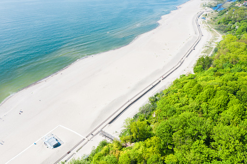 Aerial view of white wooden umbrellas and promenade on Yantarniy beach in Kaliningrad region.