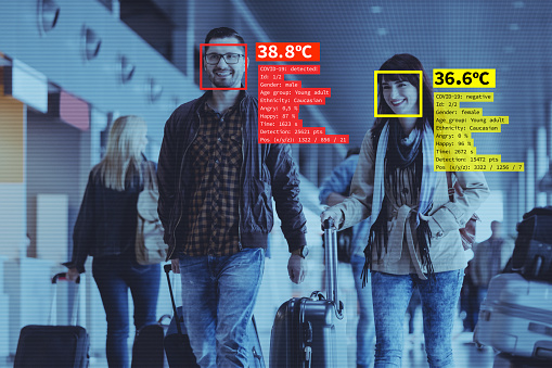 Facial recognition system at the airport during covid-19 pandemic, measuring temperature. People carrying luggage.