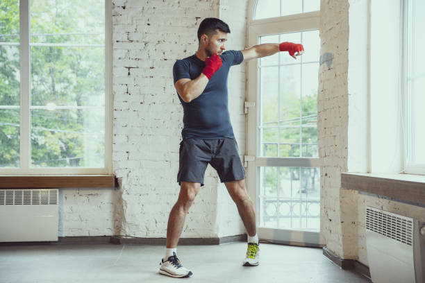 young caucasian man training at home during quarantine of coronavirus outbreak, doing exercises of fitness, aerobic. staying sportive during insulation. - healthy lifestyle men boxing dumbbell imagens e fotografias de stock