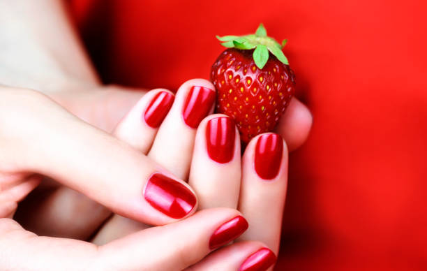 istock Female hand with red manicure holding a strawberry. 1248482103