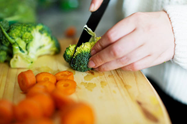 istock Woman's hands using kitchen knife to chop vegetables including carrots and broccoli 1248482346