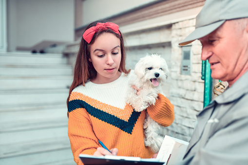 Young Female With Puppy Signing Mailman's Receipt