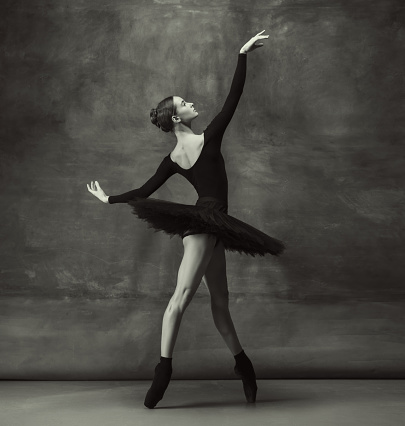 Passioned. Graceful classic ballerina dancing, posing isolated on dark studio background. Elegance black tutu. Grace, movement, action and motion concept. Looks weightless, flexible. Fashionable.