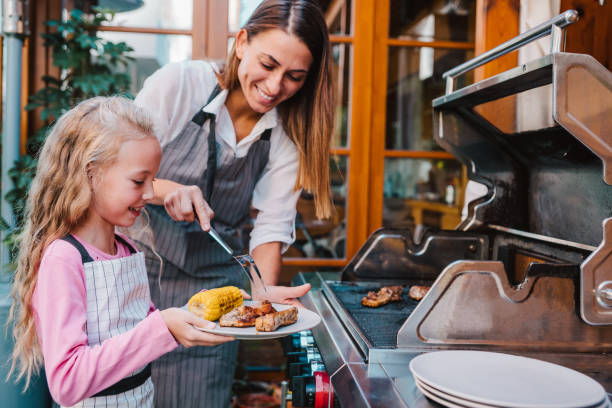 Mother and daughter making barbecue in the backyard. Young happy woman and cute cheerful girl grilling meat and corn on a barbecue grill in the backyard of their house. grilled stock pictures, royalty-free photos & images
