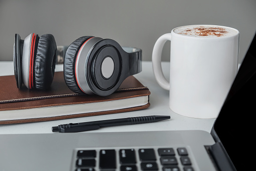 Close up shot of home office setups ,ready for morning conference call which consists of  headphones , blank paper ballpoint pen and hot mochaccino, next to laptop