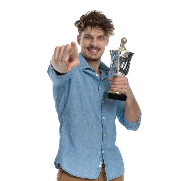 istock happy young guy pointing finger and holding trophy 1248492840
