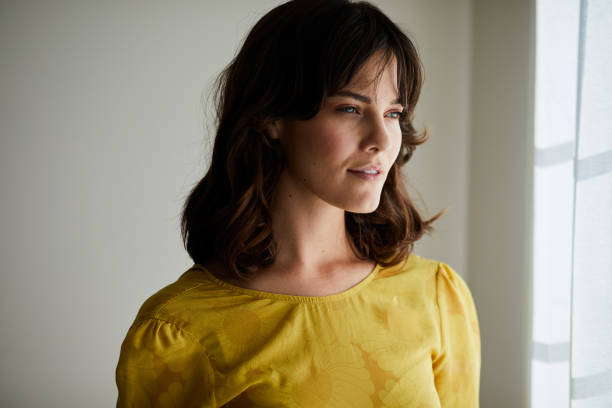 istock Young brunette woman looking out through a window at home 1248492842