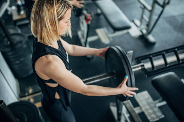 istock Strong woman putting weights on barbell before training in gym 1248498732