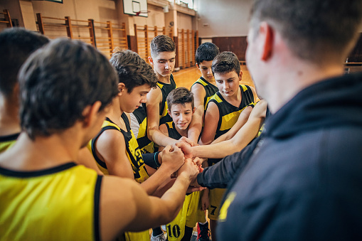 Group of young teenage boys, basketball players, with their coach huddling before the game.