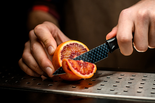 close-up bartender cuts slice of citrus with knife