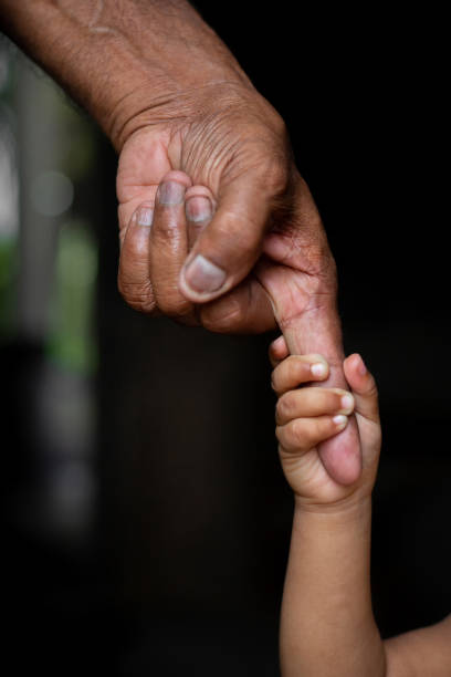 mains d’un bébé se tenant étroitement le doigt de vieillesse d’un homme aîné. concept de famille, de génération, de soutien et de personnes. fond sombre. - multi generation family adoption family human hand photos et images de collection