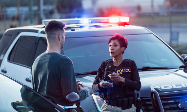 Policewoman taking a statement from young man A policewoman taking a statement from a civilian outside her patrol car. The officer is a mature African-American woman in her 40s. She is talking with a young man in his 20s. interrogation woman stock pictures, royalty-free photos & images