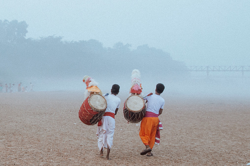 Dhaaki or drummers are integral part of Durga Puja, the biggest Hindu festival of Bengalis. This is a photo of two drummers walking on a riverbed on the first day of Durga Puja for the Nabapatrika Snan (bathing ritual).