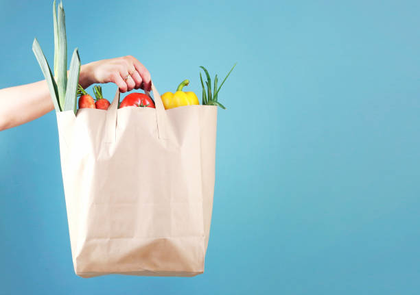 istock Hand holding paper bag with vegetables empty space blue background.Online market. 1248520004