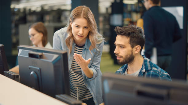 istock University Library: Bright Caucasian Girl and Talented Hispanic Boy Study for Exams As Team, Work on Assignment, Use Computer, Talk, Look for Solution, Explain Subject. College Students Work Together 1248521624