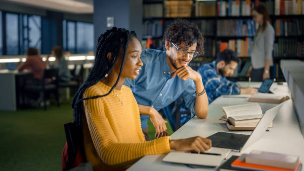 istock University Library: Gifted Black Girl uses Laptop, Smart Classmate Explains and Helps Her with Class Assignment. Happy Diverse Students Talking, Learning, Studying Together for Exams 1248521696